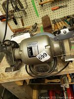 Photo of the bench grinder showing the full motor body with a label and grinding wheels on a wooden workbench.