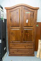 Front view of wooden armoire showing two raised panel doors and two drawers at the bottom, one knob missing but inside drawer.