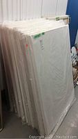 Stack of twelve white gallery canvases in plastic wrap leaning against a wall