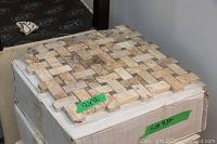 Close-up of assembled 12×12-inch beige and cream mosaic tile sheet on an unopened box labeled 12×12