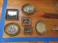Six small gold framed vintage look pictures and mirrors with floral and still life themes on wooden floor