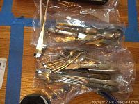 Various silverware pieces including forks, spoons, and knives laid out in plastic bags on a wooden surface.