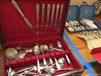 Full view of the wooden storage box containing various silverware including knives, forks, spoons, ladles, and serving spoons arranged in the red velvet slots and compartments.