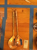 Two large ornate copper spoons showing full length with decorative handles and hammered bowls.
