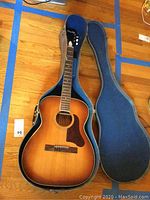 Full view of the Barclay acoustic guitar inside its open hard case showcasing the sunburst finish and tortoiseshell pickguard.