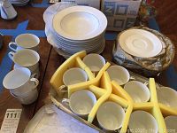 Overall view of the lot showing stacked shallow soup bowls, tea cups, padded storage trays, and boxed saucers.