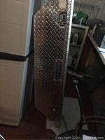 Side view of aluminum diamond plate truck bed tool box leaning against a plastic storage container.