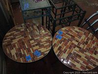 Photo showing two round patio tables with orange, red, cream ceramic tile mosaic tops and green metal bases, placed side by side.