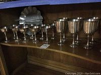 Wide view of pewter drinking glasses arranged on a shelf with a pewter tray and tongs behind them.