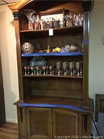 Front view of the vintage wooden bookshelf filled with glassware and decorative items on the upper shelves, showcasing its open shelving and cupboard below