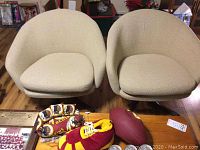 Front view of two beige swivel chairs and maple coffee table with miscellaneous items on top