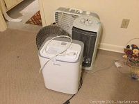 Three items placed on carpet floor against wall: Hisense dehumidifier front and center, white space heater and black metal fan behind.
