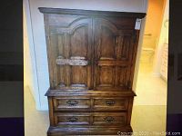 Front view of vintage wooden armoire with two paneled doors and four drawers, showing metal handles and carved wood design.