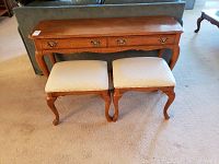 Front view of medium brown wood stain couch table paired with two matching stools featuring cream upholstered seats on curved legs.