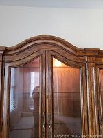 Close-up of the upper decorative curved molding and double glass doors showing wooden frame detail and brass handles.