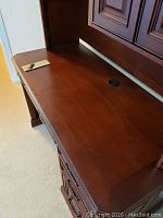 Top flat work surface of the cherry finish desk with a cable management hole and keys placed on top.