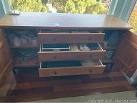 Closed wooden sideboard cabinet containing table linens, serving dishes, and candles.