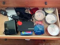 Drawer with two external hard drives, multiple stacks of DVD-R discs in spindle cases, and accessories including cables and pouches.