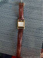 Full view of the Hamilton wristwatch showing the leather strap and rectangular gold-tone watch face on a textured surface.