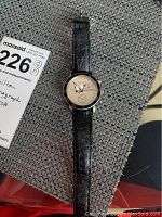 Hamilton wristwatch laying flat on a textured surface, showing black leather strap and round watch face with chronograph functions.