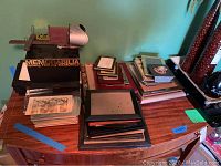 Photo of an antique stereoscope on top of a box labeled Memorabilia, surrounded by multiple photo frames and picture cards on a wooden surface.