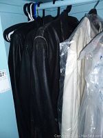 Four leather jackets hung on hangers inside a closet, mostly black with one off-white jacket partially covered in plastic.