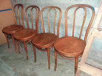 Four wooden bentwood chairs arranged in a row showing curved backs, round seats and signs of wear.