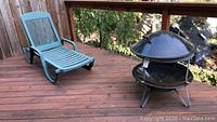 Wide view of green lounge chair and black metal fire pit on wooden deck outdoors
