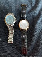 Two wristwatches placed side by side on a dark fabric surface, showing overall condition and appearance.