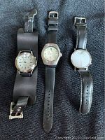 Three men's watches laid out on dark fabric: Club Room, Seiko Kinetic, and Daniel Will Harris.
