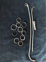 Top view of 11 rings arranged in a cluster next to 2 silver bracelets and 1 clip on dark fabric background.