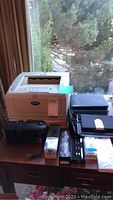 Photo showing Brother printer, black keyboards, and electronic accessories on table near window.