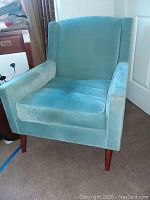 Front view of the light blue upholstered accent chair showing the seat cushion, armrests, and tapered wooden legs.