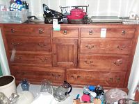 Photo of wooden dresser with multiple drawers, medium wood finish and metal hardware, with items on and around it not included in sale.