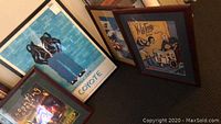 Four framed art prints leaning against a surface, including visible 'Coyote' poster with anthropomorphic wolf figure in leather jacket.