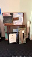 9 pieces of wall art and a mirror arranged leaning against wall showing various frame styles and sizes including a framed diploma.