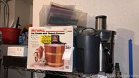 Photo showing boxed Rival Ice Cream and Yogurt Freezer on top left, Breville juicer, Keurig brewer, and clear storage boxes on right.