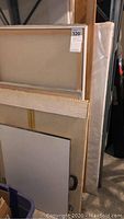 View of stacked framed canvases and wood frames of various sizes with wooden edges visible