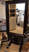 Front view of the large floor mirror reflecting a closet area, showing the dark wooden frame and stand.