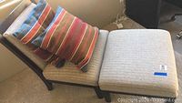 Photo of beige upholstered lounge chair with dark wood frame and legs, showing one striped pillow on seat