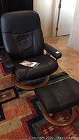 Full view of black leather Ekornes Stressless chair and ottoman on multicolor rug