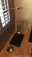 Photo of glass top side table next to a brushed metal floor lamp with adjustable lamp head