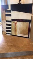Full view of the large abstract geometric canvas painting leaning against a wall on a tiled floor.
