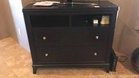 Black wooden nightstand with two drawers and open compartments on tiled floor.
