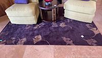 Full view of rug under chairs and small table showing purple base color with beige wave-like abstract shapes.