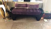 Front view of dark wooden bench with amethyst cushion and two throw pillows
