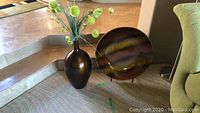 Image shows a dark brown vase beside a decorative plate on a black metal stand on the floor near steps.