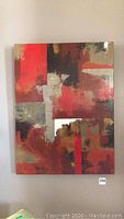 Front view of abstract painting in red, orange, gold and taupe on wall