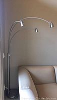 Full view of lamp next to sofa, showing three arched metal arms and conical LED heads.