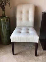 Front view of one chair showing button-tufted back and seat, dark wood legs.